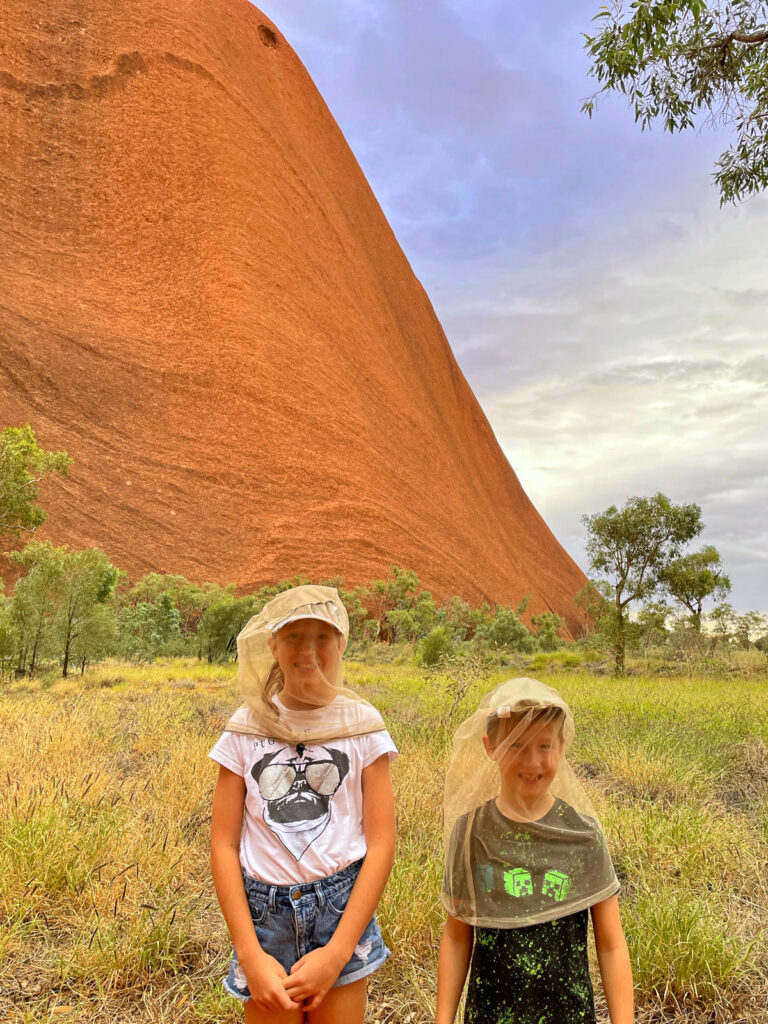 Kids wearing fly nets in front of Uluru