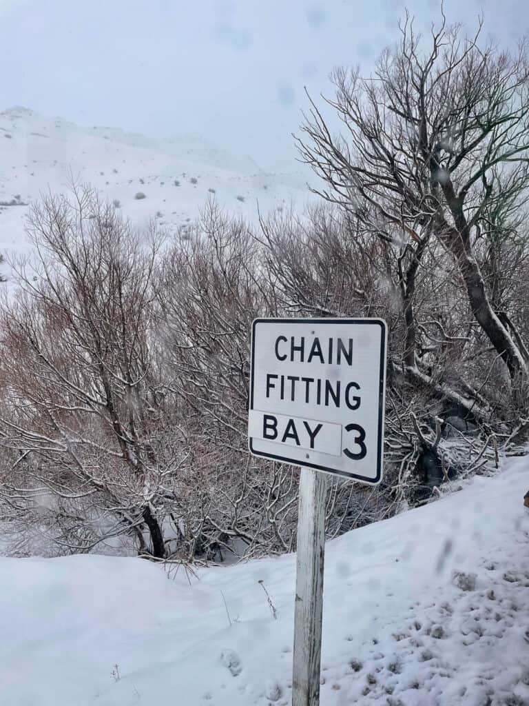 Sign for chain fitting bay on road to Remarkables with snow on the trees. 